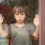 Little boy behind the window in the rain