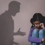 Crying little girl near beige wall, space for text. Domestic vio