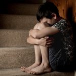 Sad, bullied or abused boy crying sitting on stairs