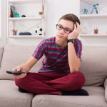 Boy watching tv and looking bored on couch at home