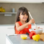 cheerful-girl-tossing-salad-bowl-with-big-wooden-spoon-cute-child-spending-time-home-pandemic-cooking-vegetables-posing-smiling-camera-learning-cook-concept_74855-6807